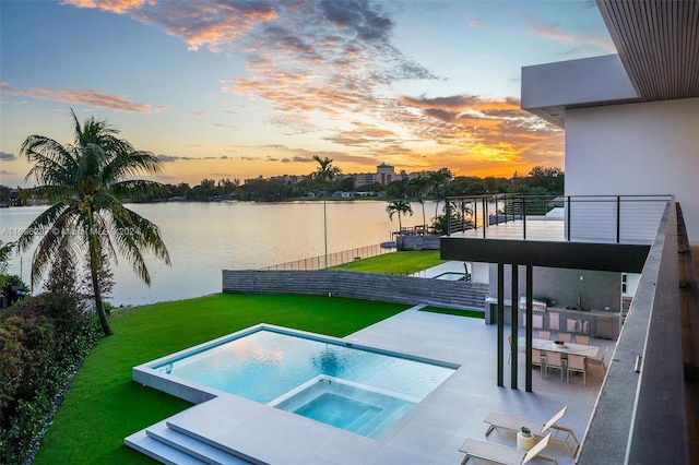 pool at dusk featuring a water view, a yard, and an in ground hot tub