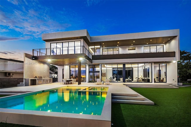 back house at dusk featuring an outdoor kitchen, a balcony, and a patio