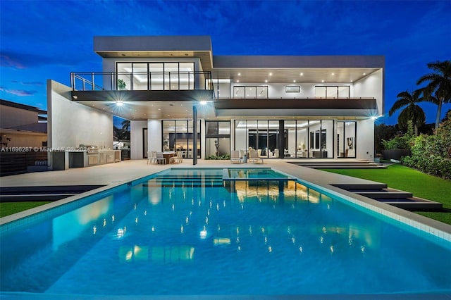 back house at night featuring a patio area, a balcony, and exterior kitchen