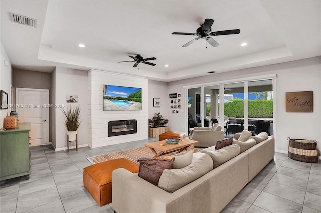 living room with a tray ceiling, ceiling fan, and a large fireplace