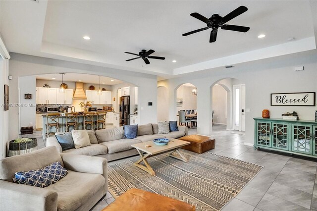 living room featuring a tray ceiling, ceiling fan, and light tile patterned floors