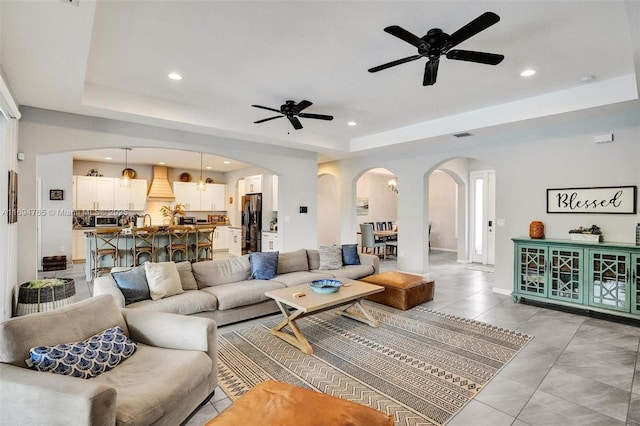 living room with light tile patterned floors, ceiling fan, and a raised ceiling