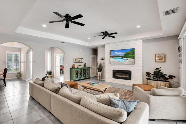 living room featuring a fireplace, light tile patterned floors, a tray ceiling, and ceiling fan