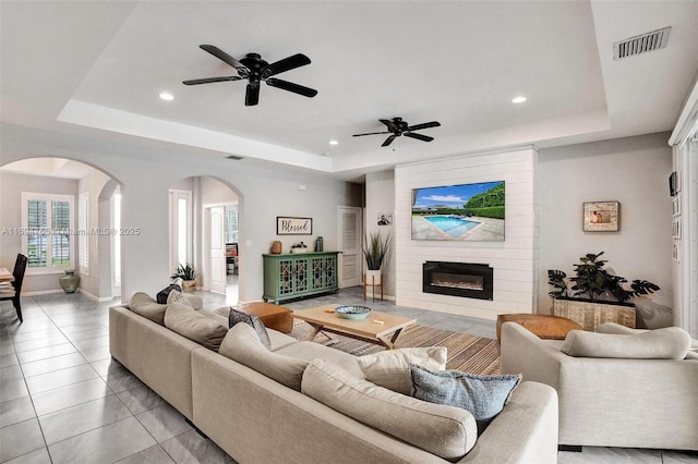 living room featuring ceiling fan, light tile patterned floors, a tray ceiling, and a fireplace