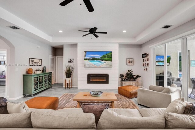 living room with a raised ceiling, ceiling fan, and a fireplace