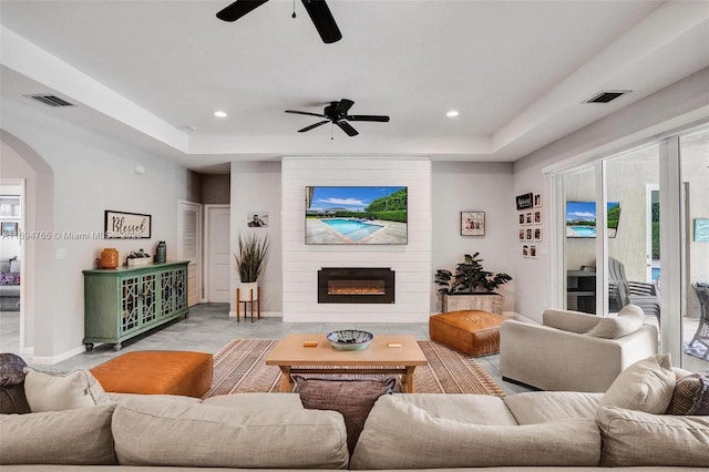 living room featuring a fireplace, a tray ceiling, and ceiling fan