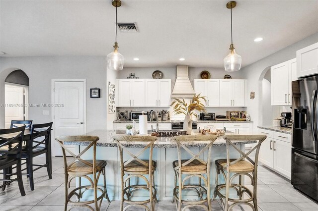 kitchen with refrigerator with ice dispenser, pendant lighting, a center island with sink, and light stone counters