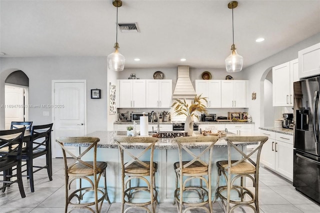 kitchen with a kitchen island with sink, light stone countertops, fridge with ice dispenser, and pendant lighting