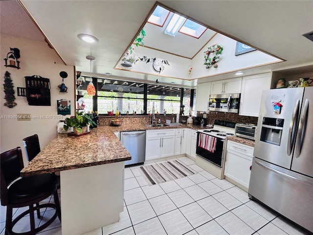 kitchen with white cabinetry, kitchen peninsula, a kitchen bar, vaulted ceiling with skylight, and appliances with stainless steel finishes