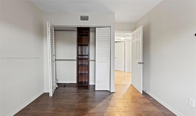 unfurnished bedroom featuring dark hardwood / wood-style floors, a textured ceiling, and a closet