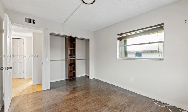 unfurnished bedroom featuring dark hardwood / wood-style flooring, a textured ceiling, and a closet