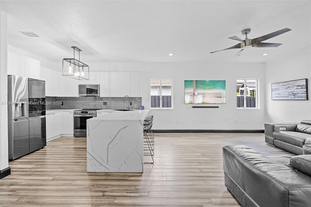 kitchen featuring decorative backsplash, appliances with stainless steel finishes, light stone countertops, decorative light fixtures, and white cabinets