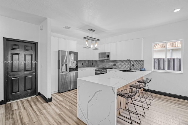 kitchen featuring white cabinetry, sink, stainless steel appliances, backsplash, and decorative light fixtures