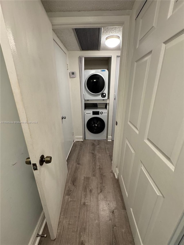 hallway featuring stacked washing maching and dryer, a textured ceiling, and hardwood / wood-style flooring