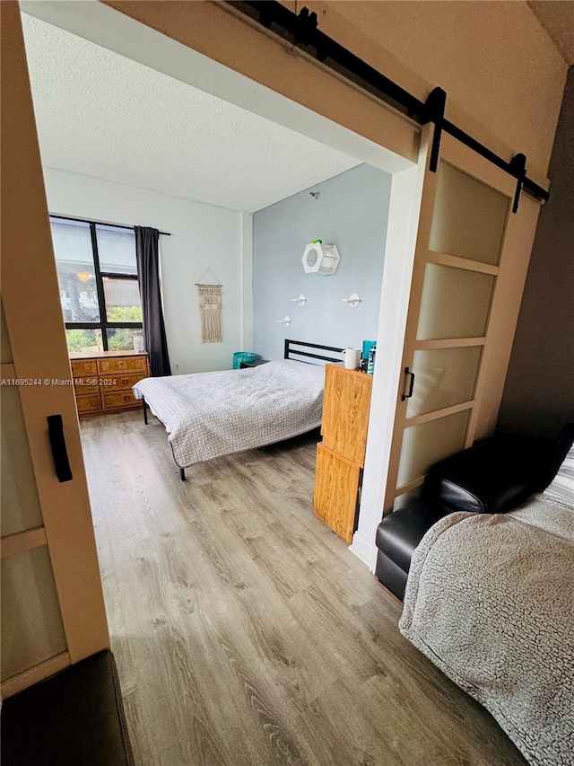 bedroom with a barn door, light hardwood / wood-style flooring, and a textured ceiling