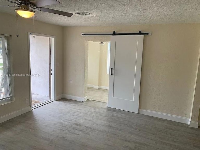 unfurnished room with hardwood / wood-style floors, a barn door, a textured ceiling, and ceiling fan