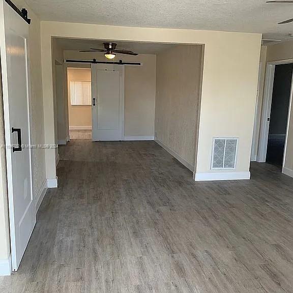 unfurnished room featuring ceiling fan, a barn door, dark hardwood / wood-style flooring, and a textured ceiling