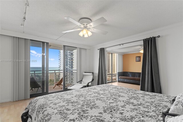 bedroom with ceiling fan, access to outside, a textured ceiling, crown molding, and a water view