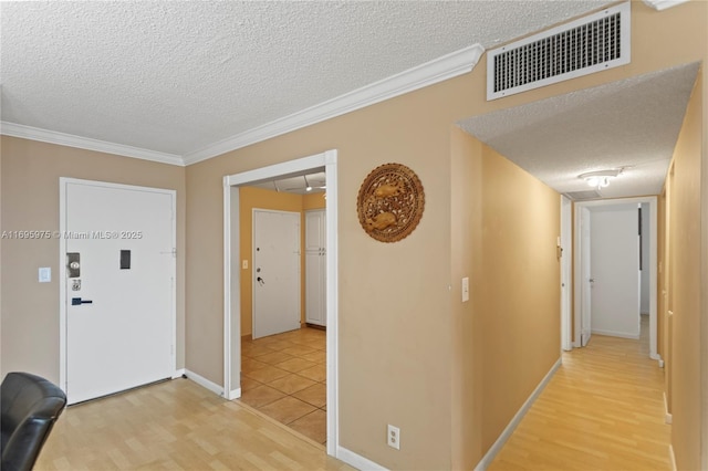 corridor with light wood-type flooring, ornamental molding, and a textured ceiling