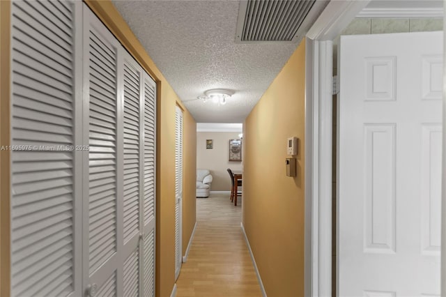 hallway with a textured ceiling and light hardwood / wood-style flooring