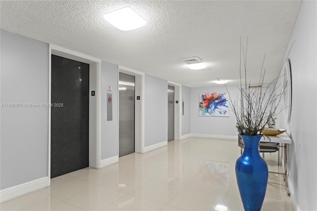 hallway featuring light tile patterned flooring, a textured ceiling, and elevator