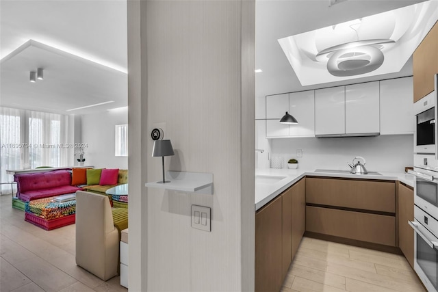 kitchen with white oven, white cabinetry, light hardwood / wood-style flooring, and stainless steel oven