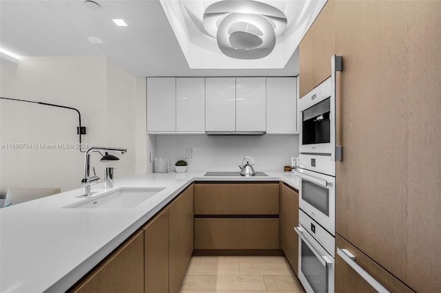 kitchen featuring light wood-type flooring, black cooktop, double oven, sink, and white cabinetry