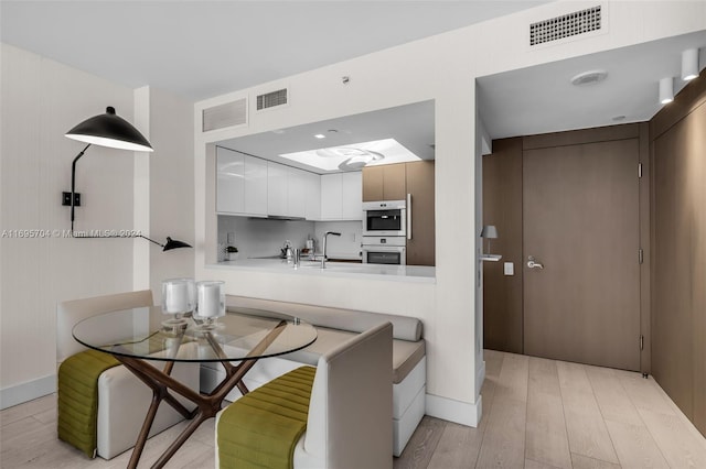 kitchen with kitchen peninsula, backsplash, double oven, light hardwood / wood-style floors, and white cabinetry