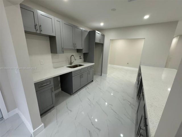 kitchen featuring gray cabinets, light stone countertops, and sink