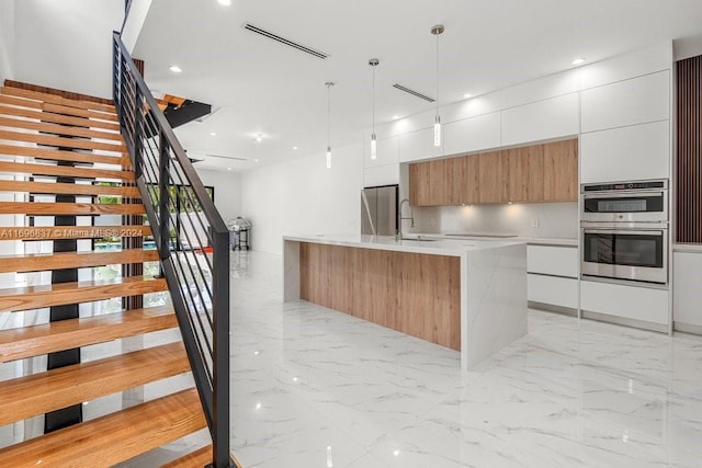 kitchen with pendant lighting, a kitchen island with sink, white cabinets, sink, and appliances with stainless steel finishes