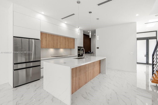 kitchen featuring white cabinets, light stone countertops, an island with sink, decorative light fixtures, and stainless steel appliances