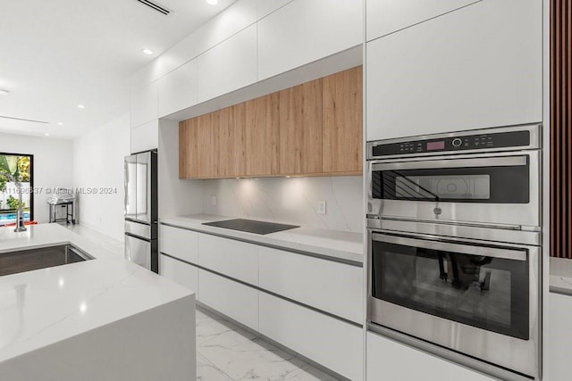 kitchen featuring light stone counters, stainless steel appliances, sink, light brown cabinets, and white cabinets