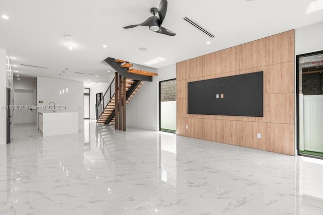 unfurnished living room with ceiling fan and wooden walls