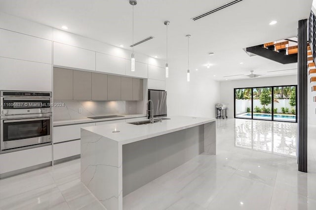 kitchen with sink, hanging light fixtures, gray cabinets, a kitchen island with sink, and appliances with stainless steel finishes