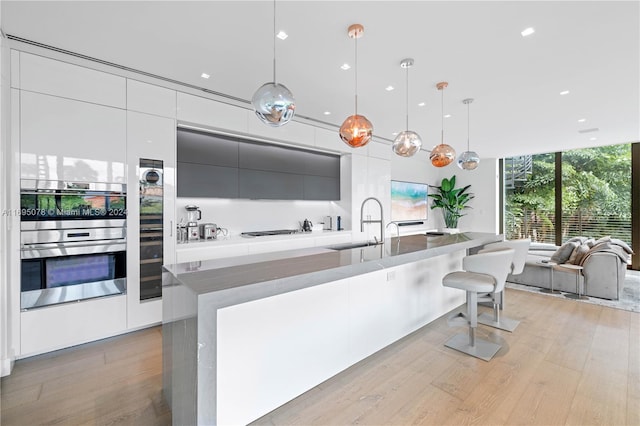 kitchen with white cabinets, decorative light fixtures, double oven, a large island, and light hardwood / wood-style floors