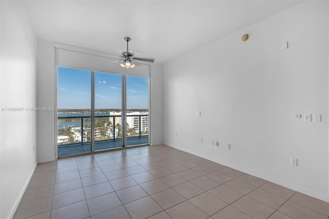 unfurnished room with light tile patterned floors, expansive windows, a water view, and a ceiling fan