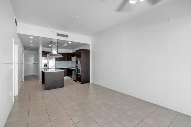 kitchen featuring visible vents, island exhaust hood, open floor plan, dark brown cabinetry, and light countertops