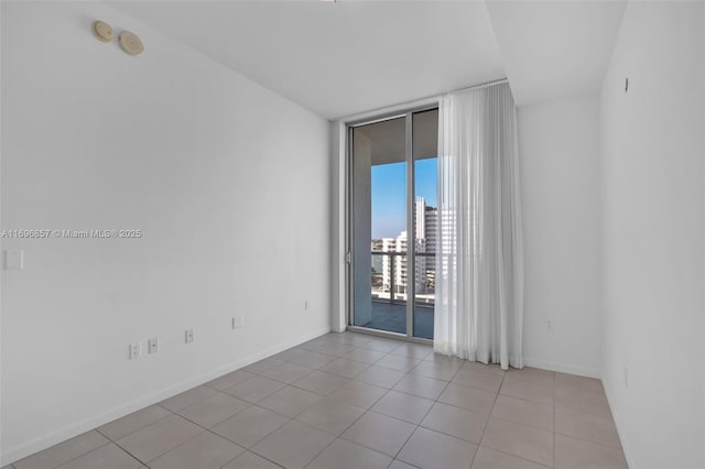 empty room featuring light tile patterned flooring, a city view, floor to ceiling windows, and baseboards