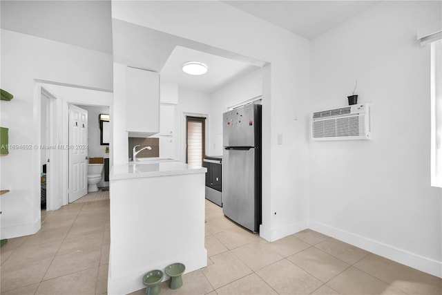 kitchen with appliances with stainless steel finishes, sink, light tile patterned floors, an AC wall unit, and white cabinets