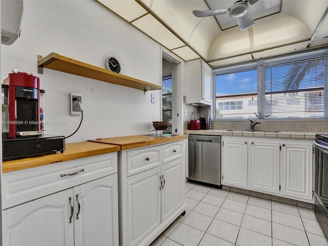 kitchen featuring stainless steel dishwasher, sink, light tile patterned floors, butcher block countertops, and white cabinetry