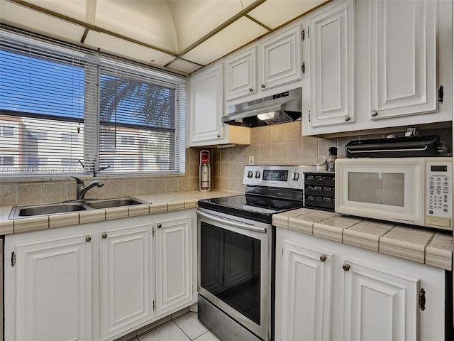 kitchen with electric range, tile counters, white cabinets, and sink