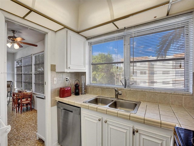 kitchen with ceiling fan, tile counters, sink, stainless steel dishwasher, and white cabinets