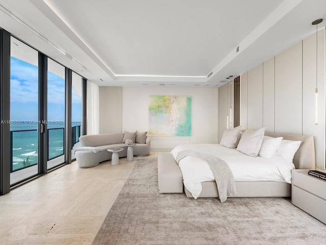 bedroom featuring access to outside, a water view, and a raised ceiling