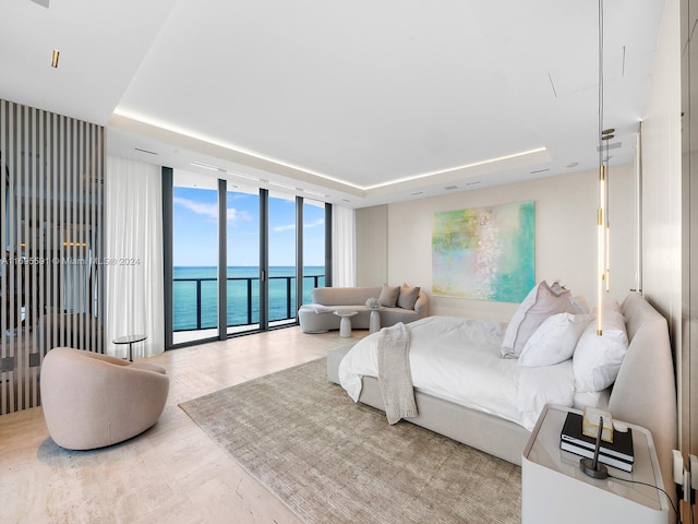 bedroom featuring access to outside, a water view, floor to ceiling windows, and a tray ceiling