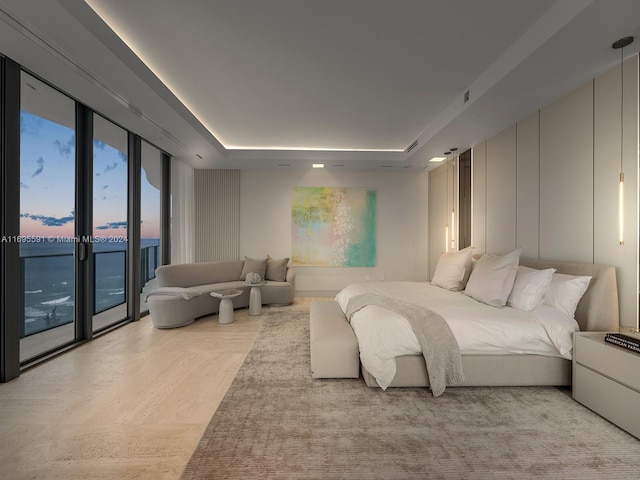 bedroom with access to outside, expansive windows, a tray ceiling, and a water view