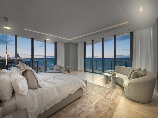 bedroom featuring a water view, a raised ceiling, expansive windows, and light hardwood / wood-style floors