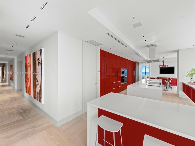 kitchen with a large island with sink, stainless steel double oven, and light wood-type flooring