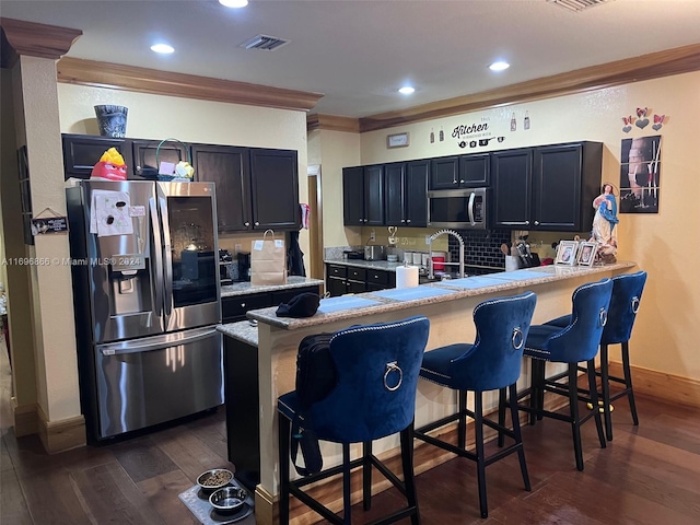 kitchen featuring a kitchen bar, kitchen peninsula, stainless steel appliances, dark wood-type flooring, and crown molding