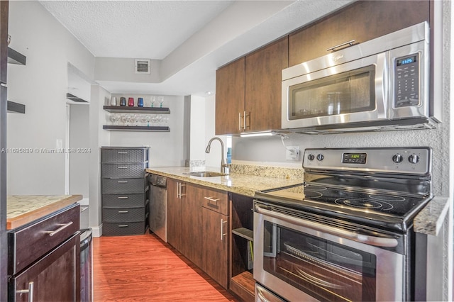 kitchen featuring sink, a textured ceiling, light stone counters, wood-type flooring, and stainless steel appliances