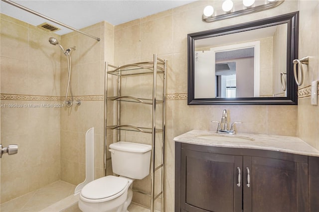 bathroom with vanity, toilet, tile walls, and a tile shower